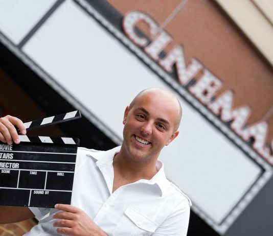 Image of a movie director holding a clapper card in front of a movie theater